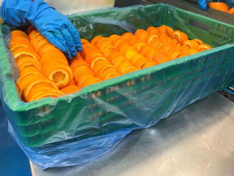 Caja de plastico verde con naranjas cortadas dentro